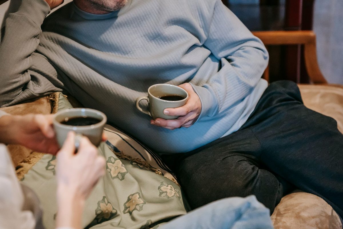 Two people on a sofa in sweatshirts holding mugs of coffee